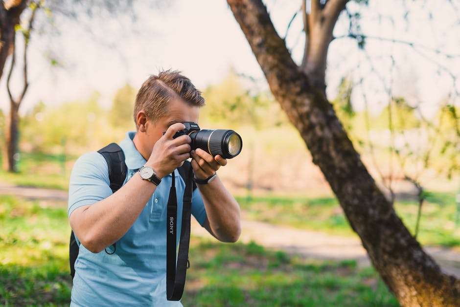 Mężczyzna w błękitnej koszulce fotografuje lustrzanką marki Sony w plenerze.