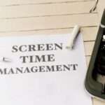 Biała kartka z napisem „SCREEN TIME MANAGEMENT” leży obok fragmentu starej maszyny do pisania.