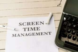 Biała kartka z napisem „SCREEN TIME MANAGEMENT” leży obok fragmentu starej maszyny do pisania.